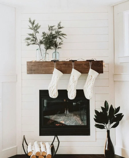 Christmas stockings hanging on a decorated fireplace with lights.